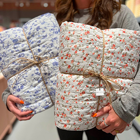 Medarbejder fra Søstrene Grene i Slagelse, holder to forskellige blomstrede tæpper fremme i butikken.