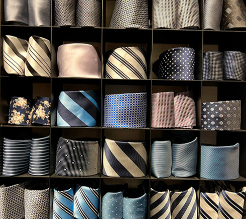 Forskellige foldede slips i blå nuancer placeret i reol hos Sams i Slagelse.